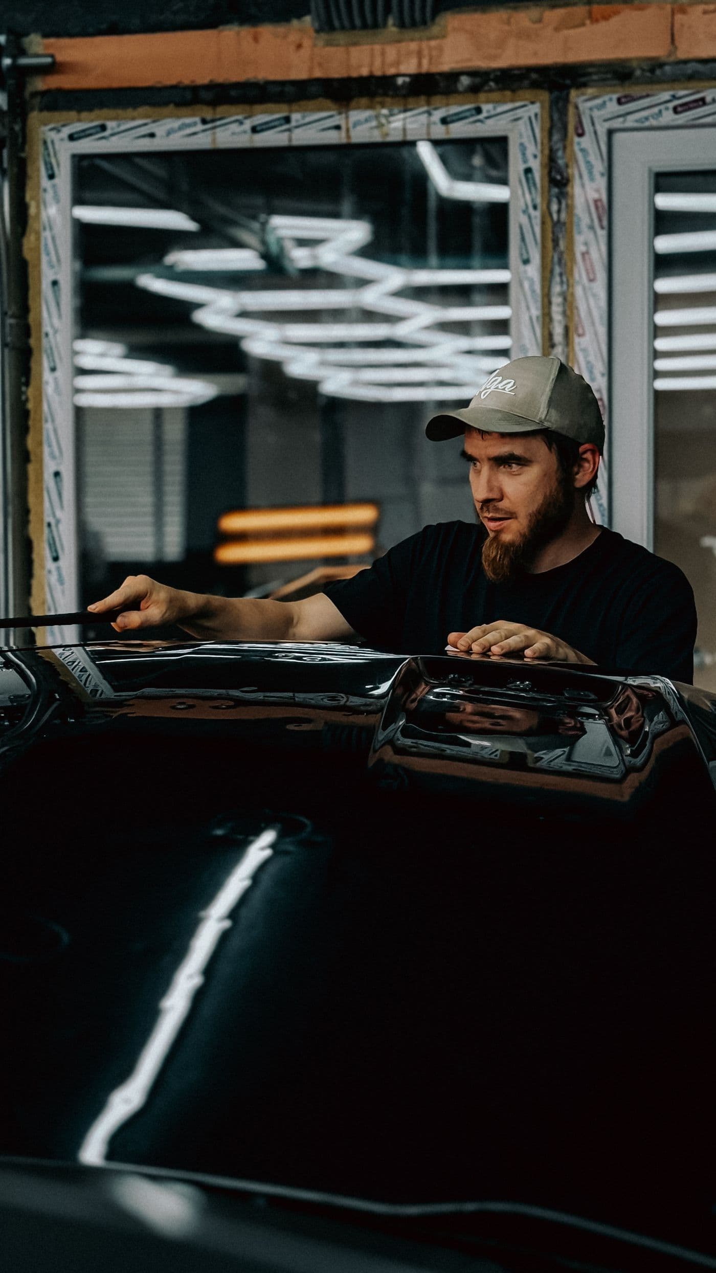 Professionnel inspectant la surface et les reflets de la carrosserie sous un éclairage d’atelier